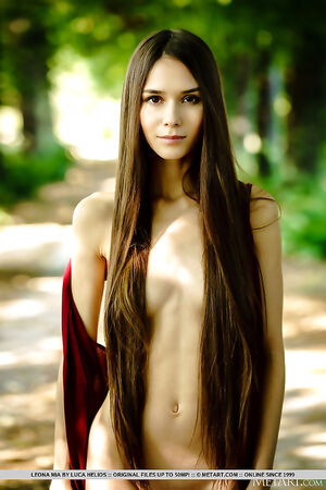 Long-haired teen beauty Leona Mia stripping nude on a park bench